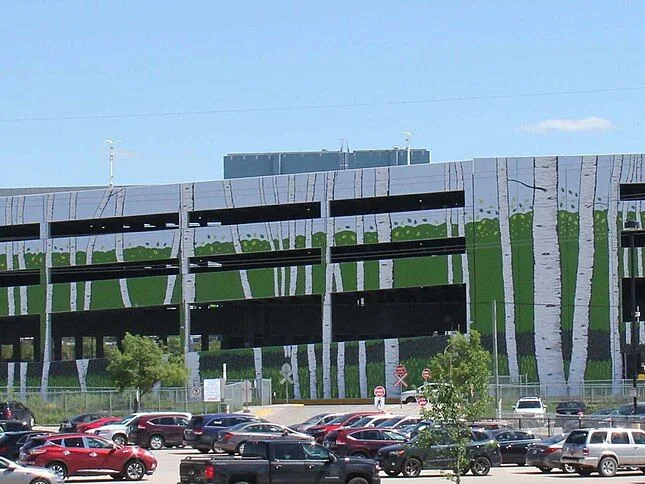 Le côté nord du complexe du Club Regent Casino à Winnipeg : le mur du stationnement étagé, orné d'une murale de bouleaux, au-dessus d'un stationnement plein